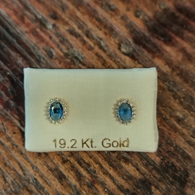 Brincos de ouro com pedras azuis em fundo branco sobre madeira