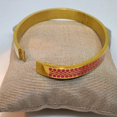 Pulseira dourada rígida com padrão rosa sobre almofada bege