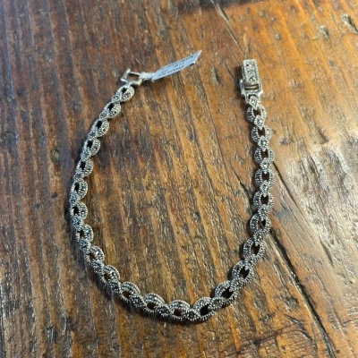 Pulseira prateada entrelaçada com etiqueta sobre mesa de madeira