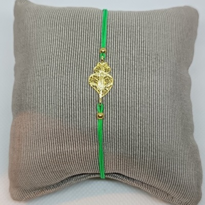 Pulseira verde com pendente dourado de coração numa almofada cinza