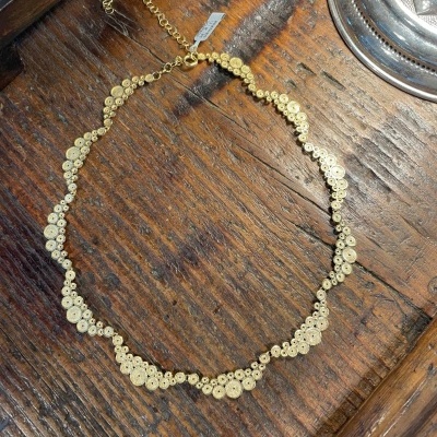 Colar dourado com peças circulares sobre mesa de madeira escura