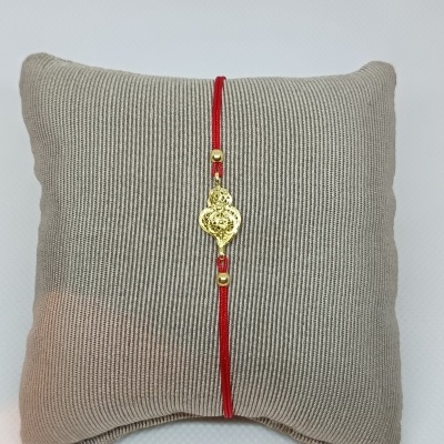 Pulseira vermelha com pendente dourado exibida numa almofada bege riscada