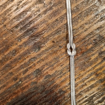 Cordão prateado com nó sobre madeira clara