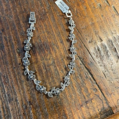 Pulseira prateada com decoração floral sobre madeira