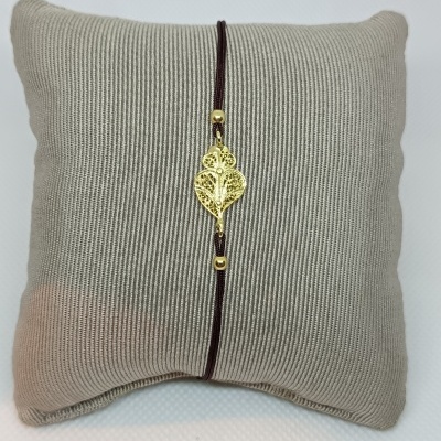 Pulseira com pendente dourado em forma de folha sobre almofada cinza