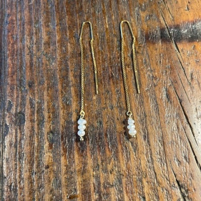 Brincos dourados com pérolas sobre mesa de madeira
