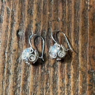 Brincos prateados com padrão espiral sobre madeira