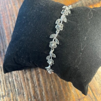 Pulseira prateada com flores e folhas sobre almofada preta