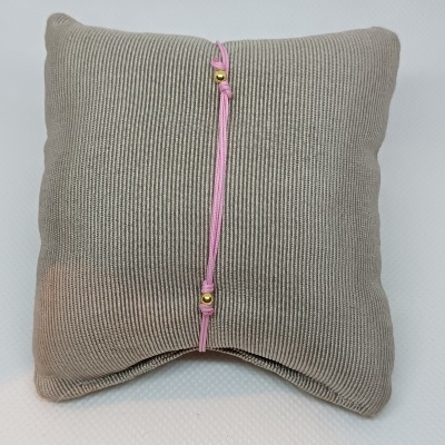 Pulseira rosa com contas douradas sobre almofada cinza texturada