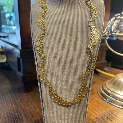 Colar dourado com padrões circulares em manequim de tecido bege