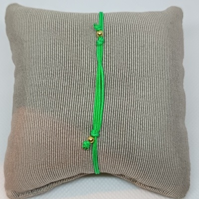 Pulseira verde com contas douradas sobre almofada cinza texturizada