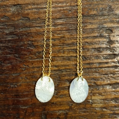 Duas correntes douradas com pendentes ovais brancos com gravuras sobre madeira
