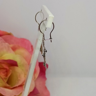 Brincos pendentes metálicos prateados exibidos na vertical com fundo de pétalas coloridas