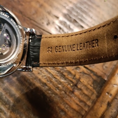 Pulseira de relógio em couro genuíno castanho com texto estampado e fundo de madeira