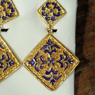 Brincos losango dourados com esmalte azul sobre tecido branco