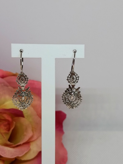 Brincos pendentes prateados em suporte branco com flor cor de rosa ao fundo