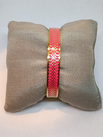 Pulseira dourada com padrão rosa numa almofada cinzenta