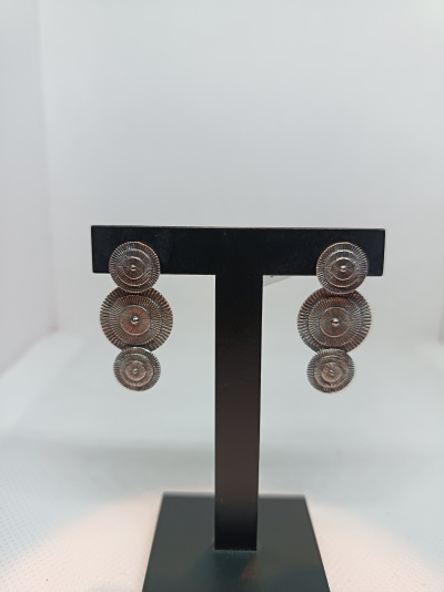 Brincos prateados com três discos texturados em suporte preto.