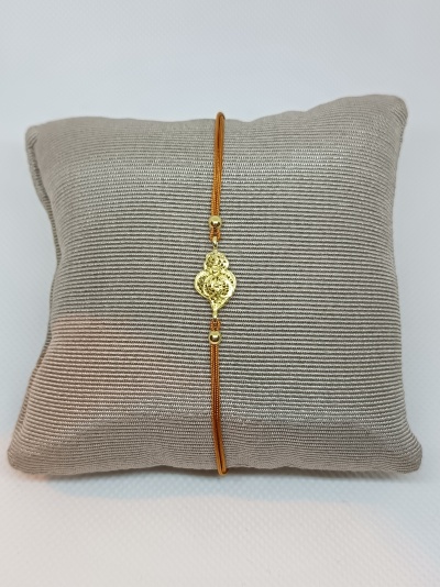 Pulseira com cordão laranja e pendente dourado sobre almofada cinza