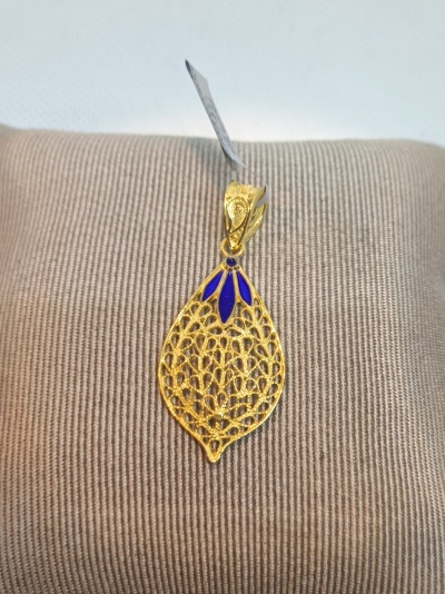 Pendente dourado em forma de folha com detalhes azuis sobre almofada bege