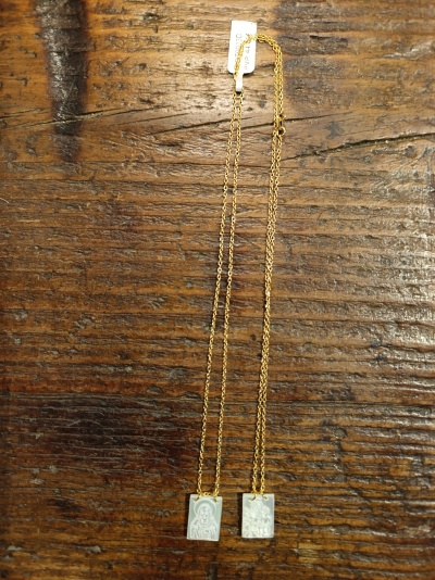 Dois colares dourados com pendentes retangulares gravados sobre madeira rústica