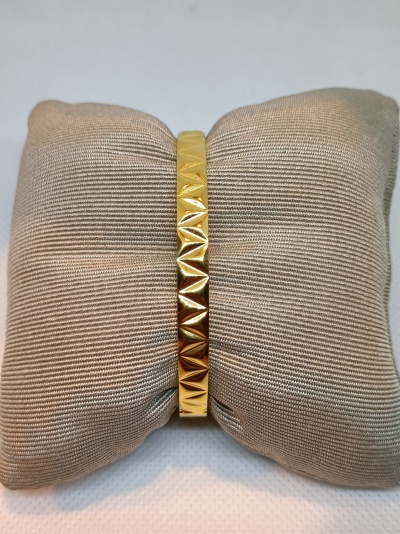 Pulseira dourada com padrão geométrico exposta numa almofada bege