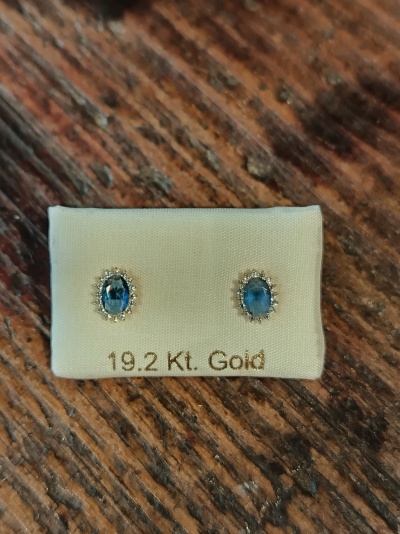 Brincos de ouro com pedras azuis em fundo branco sobre madeira