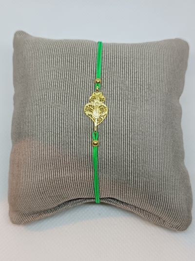 Pulseira verde com pendente dourado de coração numa almofada cinza