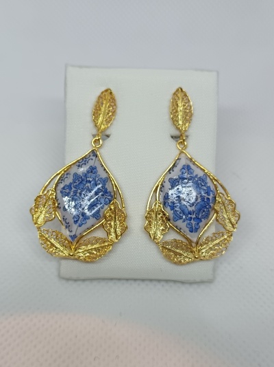 Brincos pendentes dourados com cerâmica branca e azul decorativa em forma de folha.