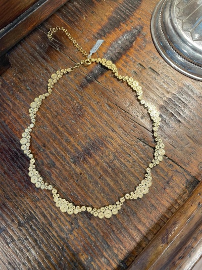 Colar dourado com peças circulares sobre mesa de madeira escura