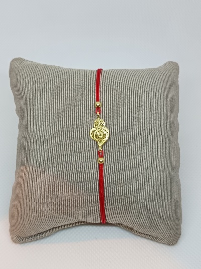 Pulseira vermelha com pendente dourado exibida numa almofada bege riscada