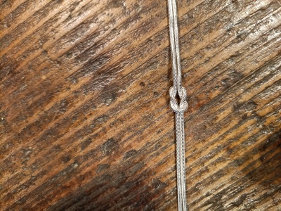 Cordão prateado com nó sobre madeira clara