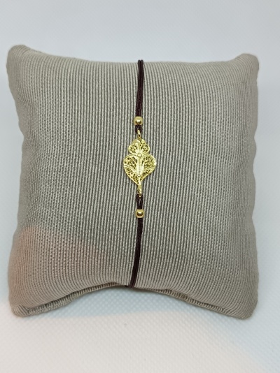 Pulseira com pendente dourado em forma de folha sobre almofada cinza