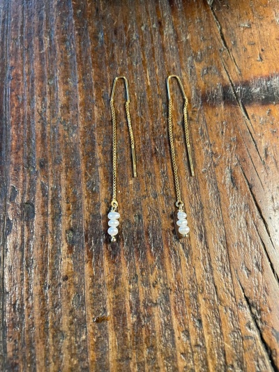 Brincos dourados com pérolas sobre mesa de madeira