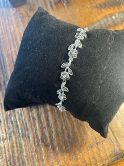 Pulseira prateada com flores e folhas sobre almofada preta