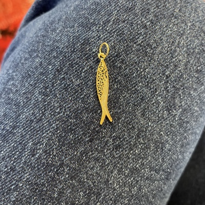 Pingente dourado em forma de peixe sobre tecido azul escuro