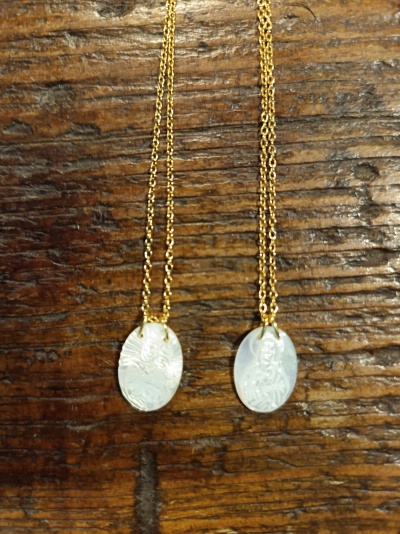 Duas correntes douradas com pendentes ovais brancos com gravuras sobre madeira