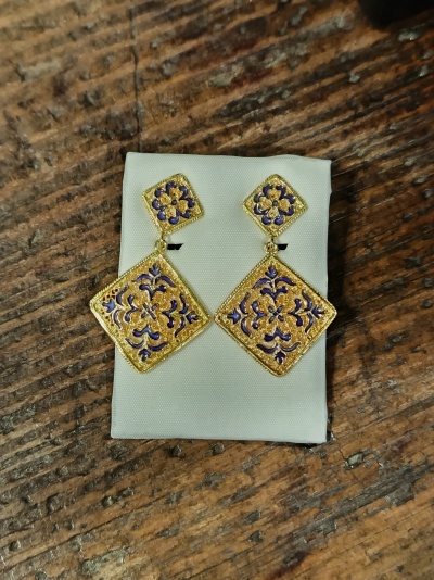 Brincos dourados com azul em forma de quadrados sobre base branca e madeira