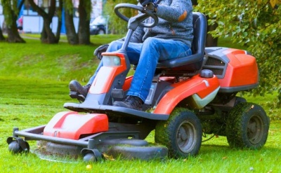 Trator de relva laranja com cortador frontal a cortar relva num parque verde.