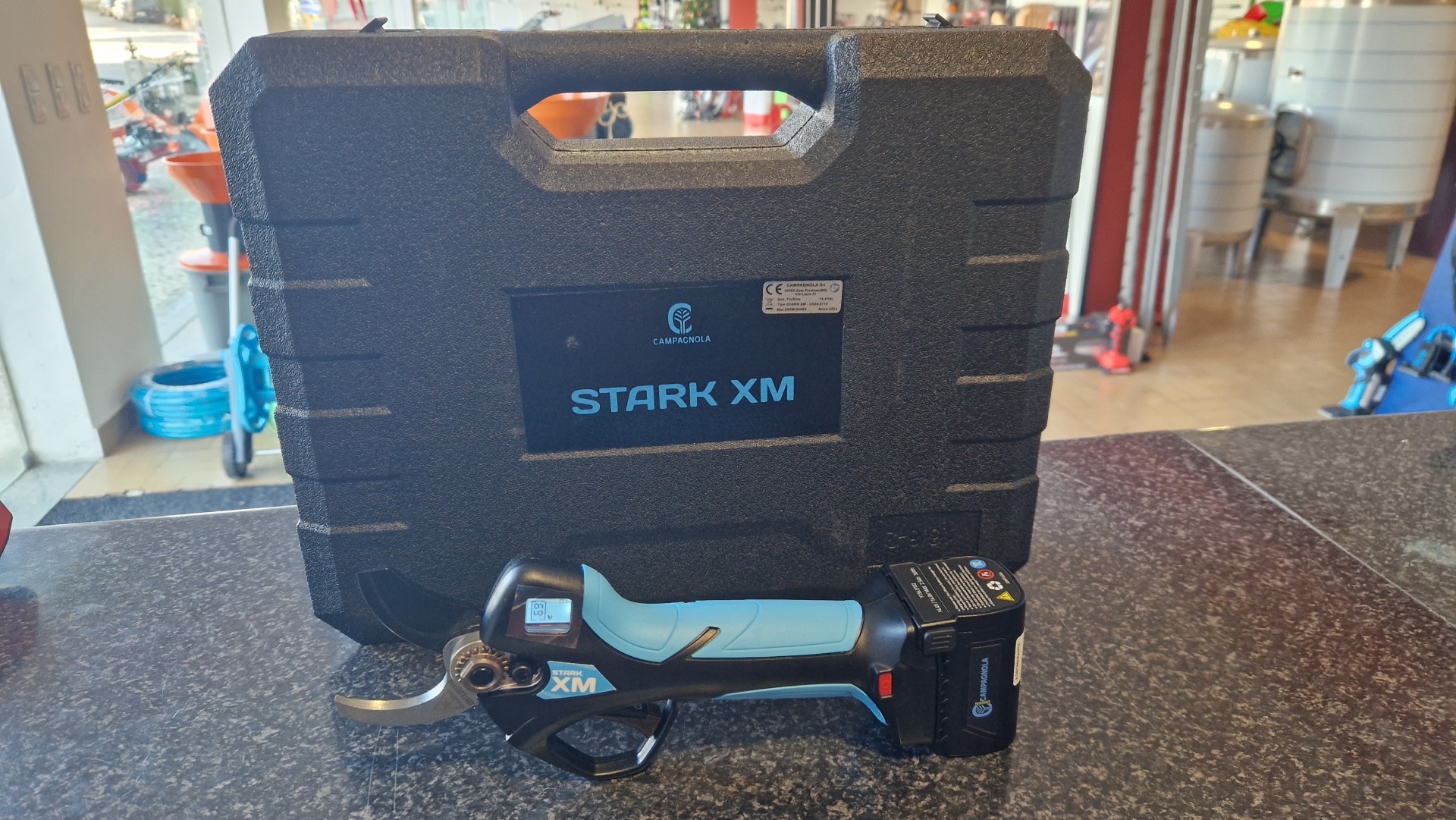 Tesoura CAMPAGNOLA STARK XM Tesoura elétrica de poda preta e azul claro com ecrã digital e estojo preto à superfície.
