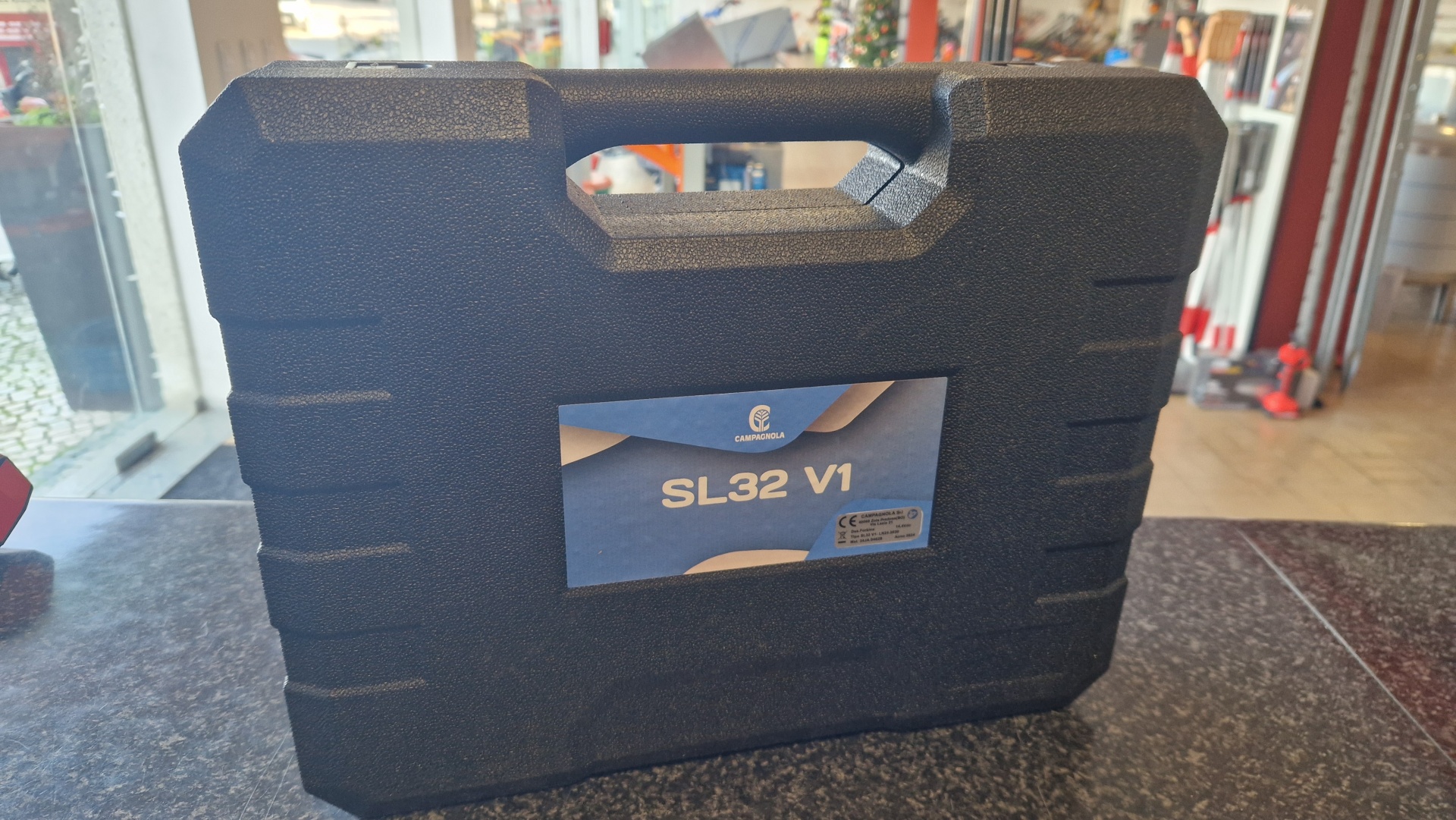 Tesoura CAMPAGNOLA SL32 V1 Estojo preto rígido com etiqueta azul 'CAMPAGNOLA SL32 V1' sobre balcão