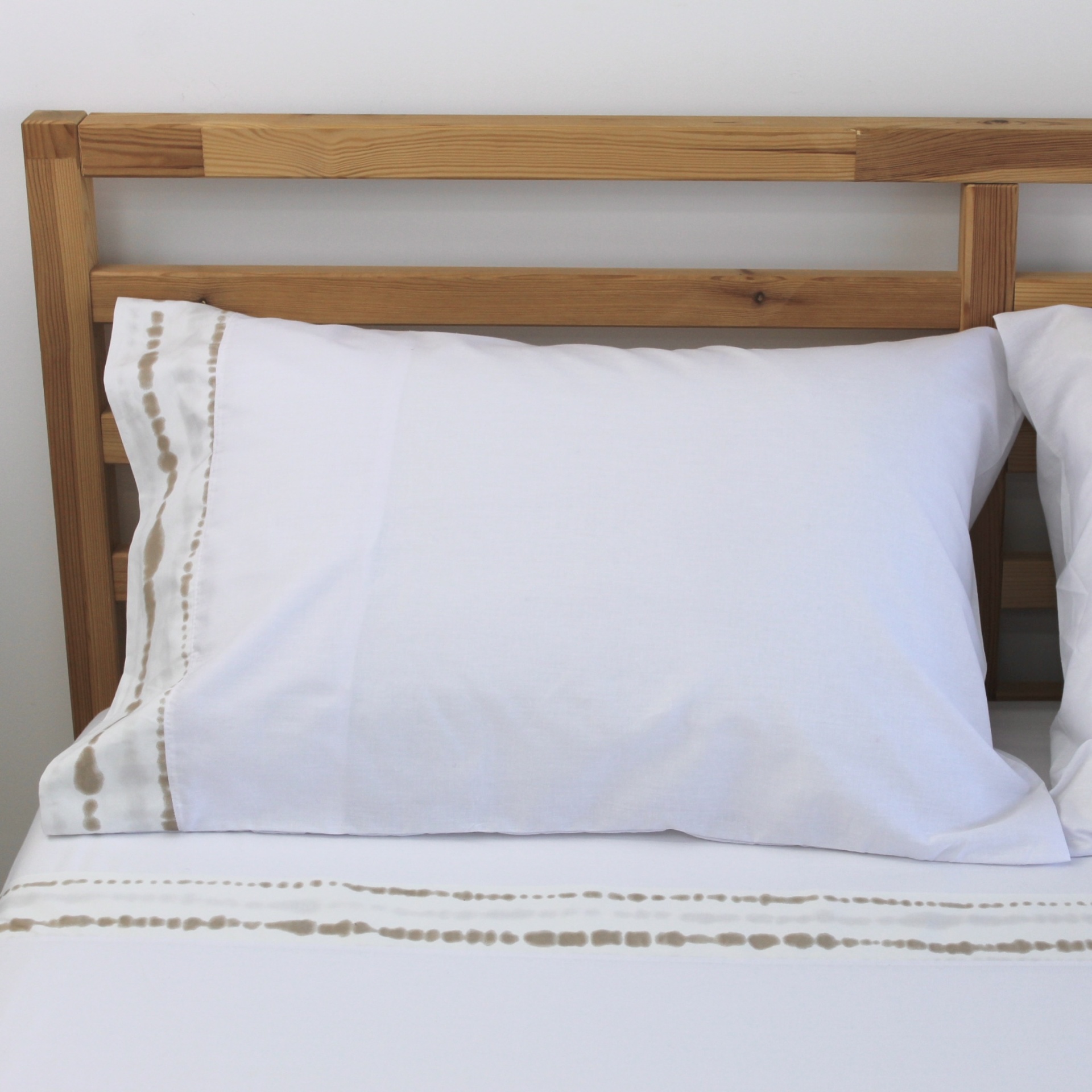 Conjunto De Lençóis Barcelos Almofada branca com bordado bege e castanho numa cama com cabeceira de madeira clara