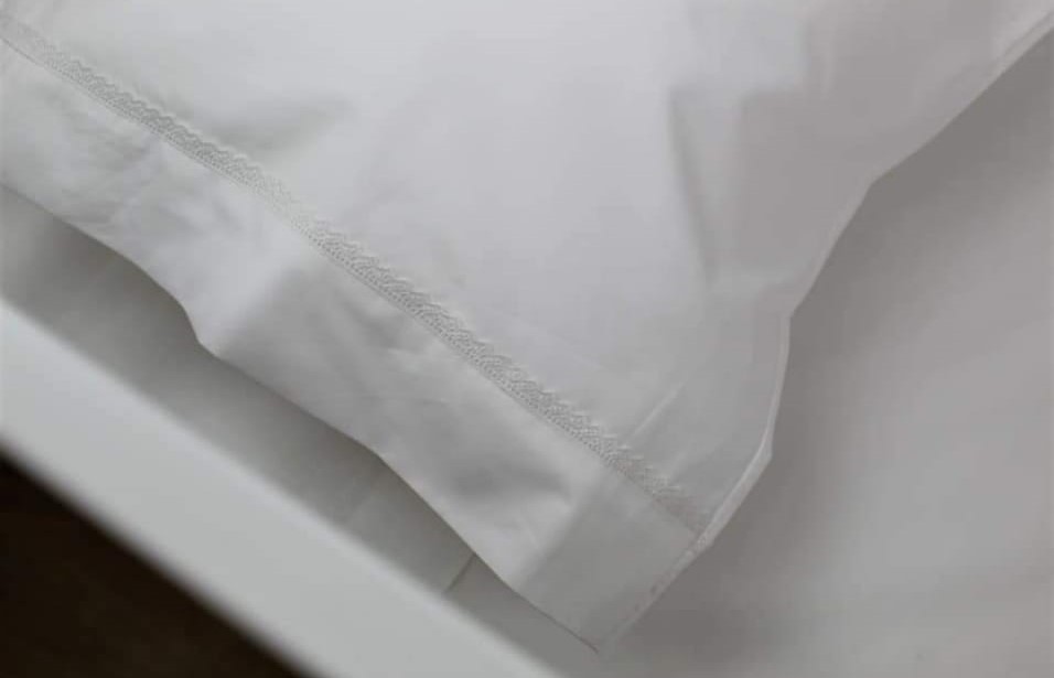 Jogo de Cama Bebé Renda Luna Travesseiro com fronha branca sobre lençol branco