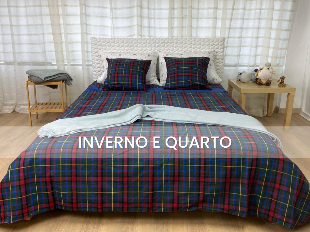 Cama com roupa de cama xadrez azul, vermelho e verde e manta clara em quarto com cortinas brancas e mesas laterais de madeira.