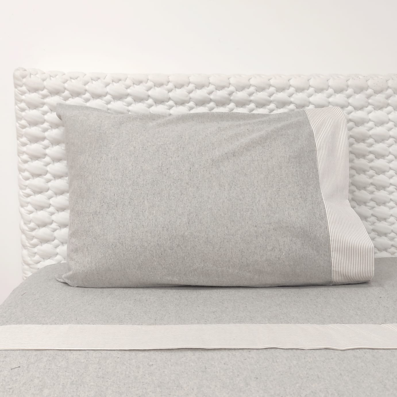 Jogo de Cama Flanela Riscas Almofada cinza claro com faixa riscada e cabeceira acolchoada branca.