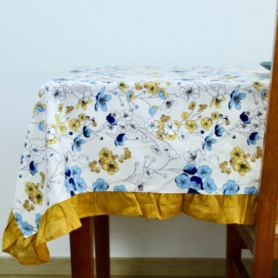 Toalha de mesa com padrão floral azul e amarelo e barra amarelo mostarda sobre mesa de madeira