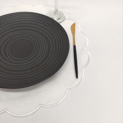 Prato preto com padrão circular, faca com cabo preto e lâmina dourada, sousplat branco ondulado e cálice de vidro