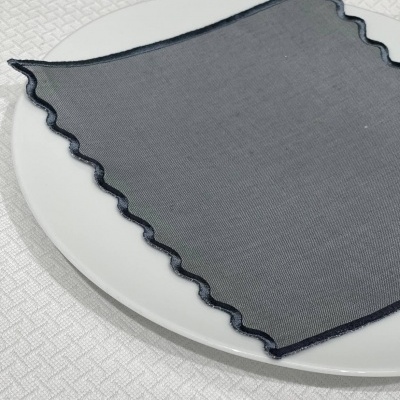 Lenço transparente cinzento escuro com bordas onduladas em prato branco