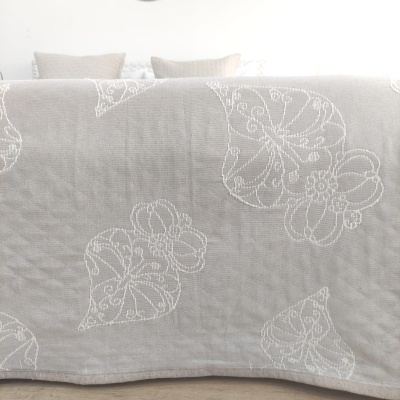 Colcha cinza com padrão de folhas brancas bordadas num quarto