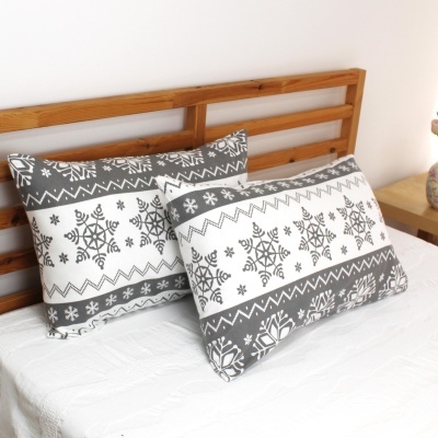Almofadas decorativas cinzentas e brancas com padrão de flocos de neve sobre cama branca e cabeceira de madeira